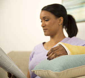 Woman reading while propping arm in cast up on pillows.