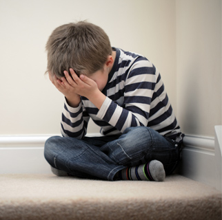 Child in a corner with his hands over his face as if afraid.