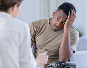 Healthcare provider talking with man, who has his hand to his forehead.