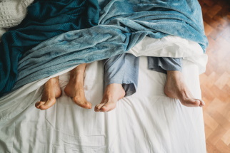 Two sets of legs sticking out of covers in a bed