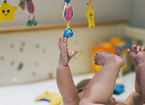 Baby girl lying in a crib reaching up to a mobile