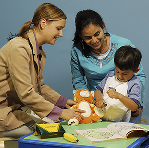 Provider and mother watching child play with medical toys.