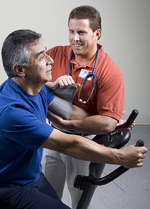 Man exercising on exercise bike while physical therapist takes his blood pressure.