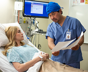 Health care provider showing printed materials to person sitting up in hospital bed.